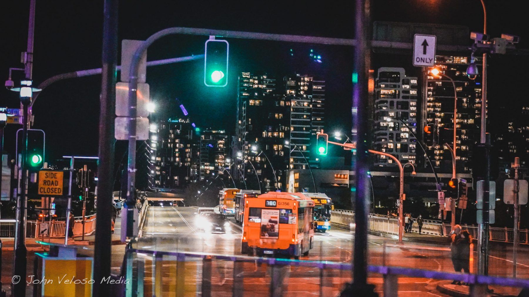 A Brisbane city intersection at night, green traffic lights and an orange bus passing through